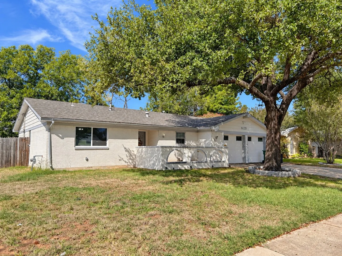 Brick exterior with a mature tree, attached garage, and a fenced yard