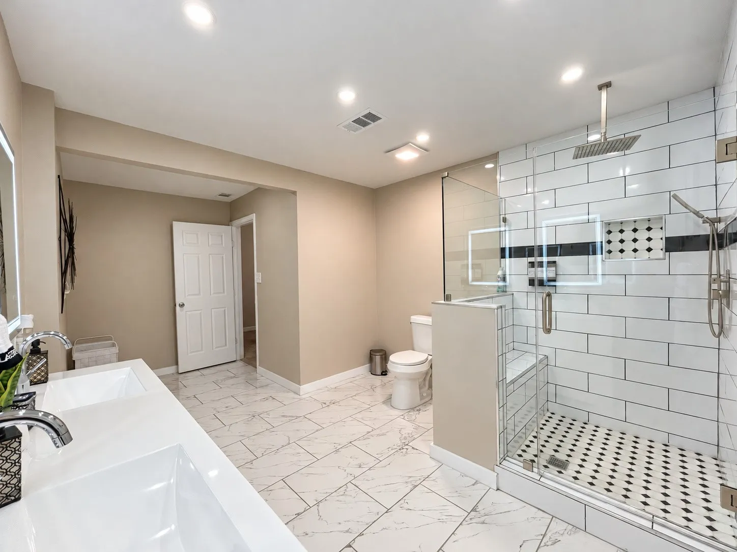 Dual vanity with undermount sinks, frameless glass shower enclosure, built-in shower bench, overhead rainfall shower fixture, and patterned shower floor tiling