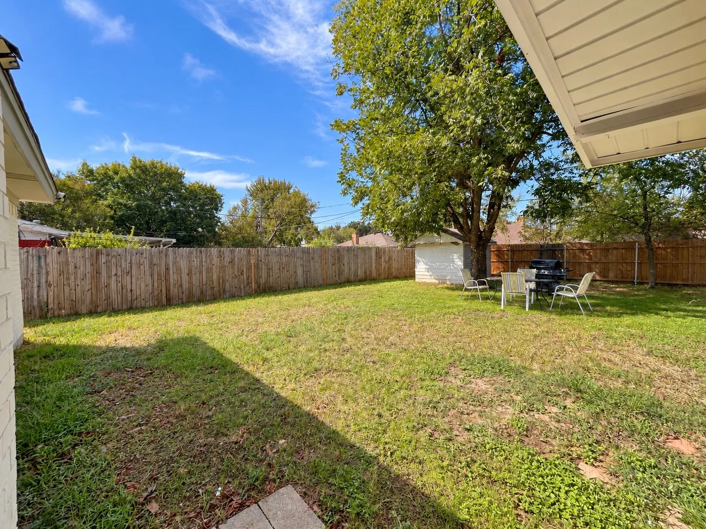 Expansive yard featuring a privacy fence, mature trees, and a detached storage shed