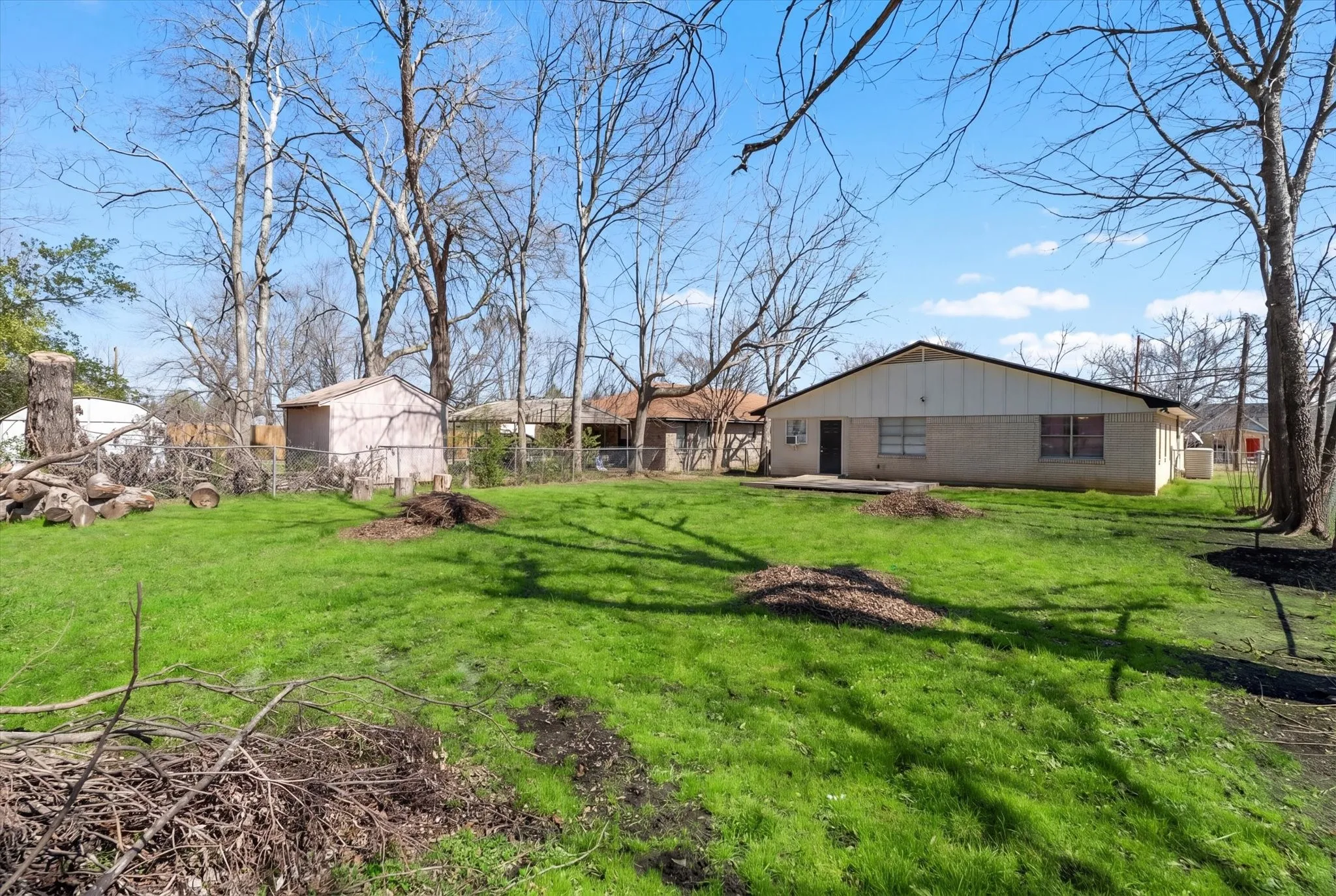 Expansive green lawn with mature trees, featuring a detached storage shed and a backyard patio