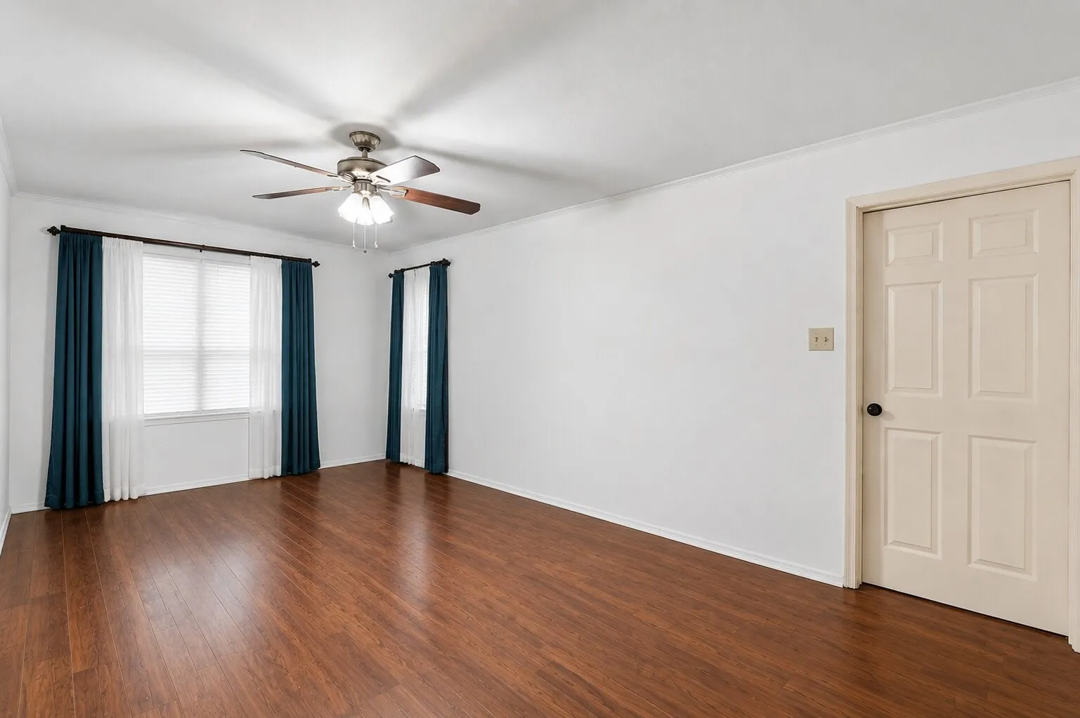 Wood-finish flooring, ceiling fan, white walls, and a multi-pane window