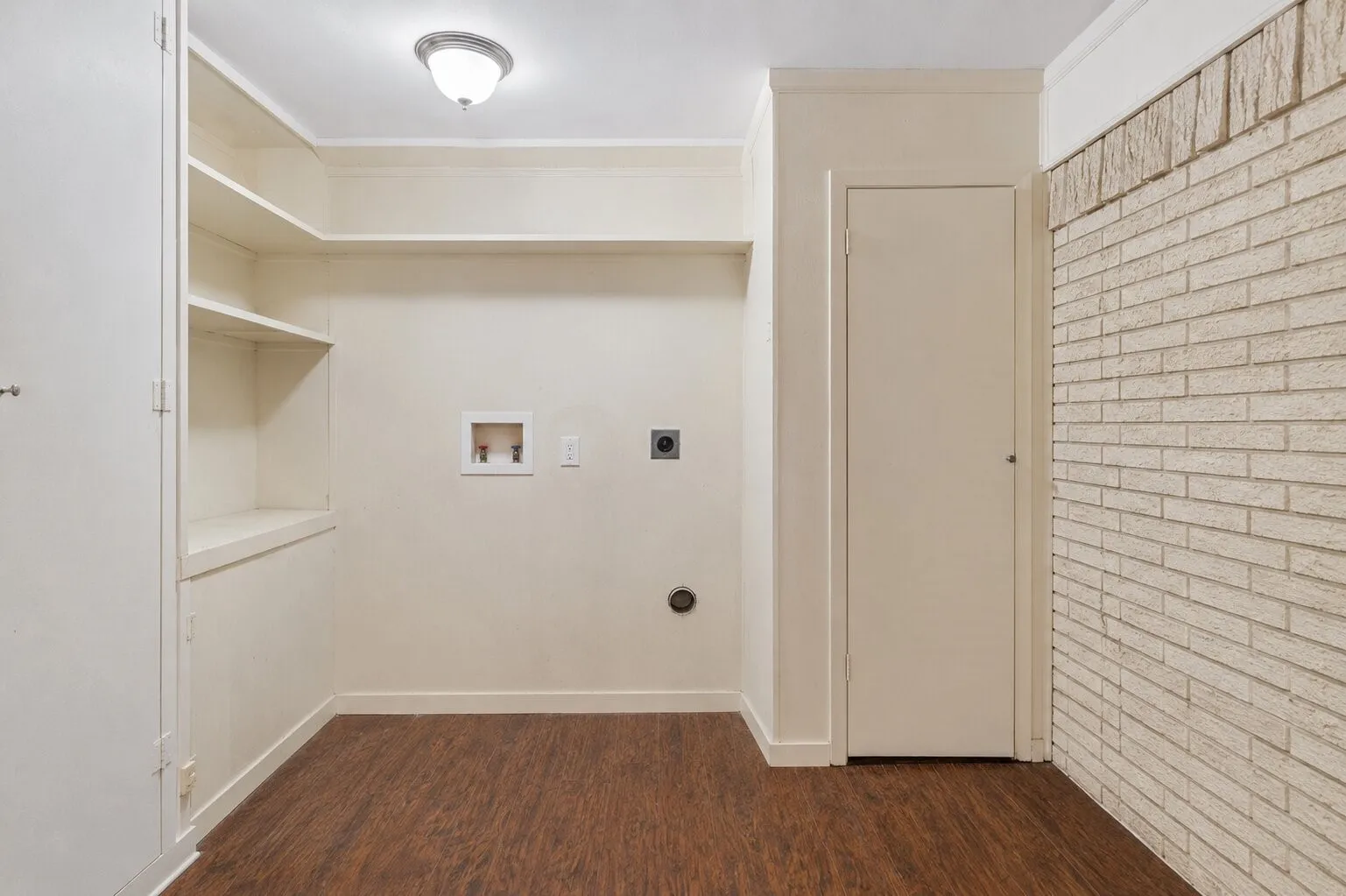 Wood-finish flooring with built-in shelving, white brick accent wall, and a flush mount ceiling light