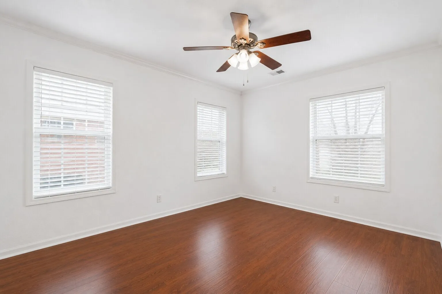 Wood-finish flooring, multiple windows with blinds, ceiling fan with integrated lighting, and crown molding