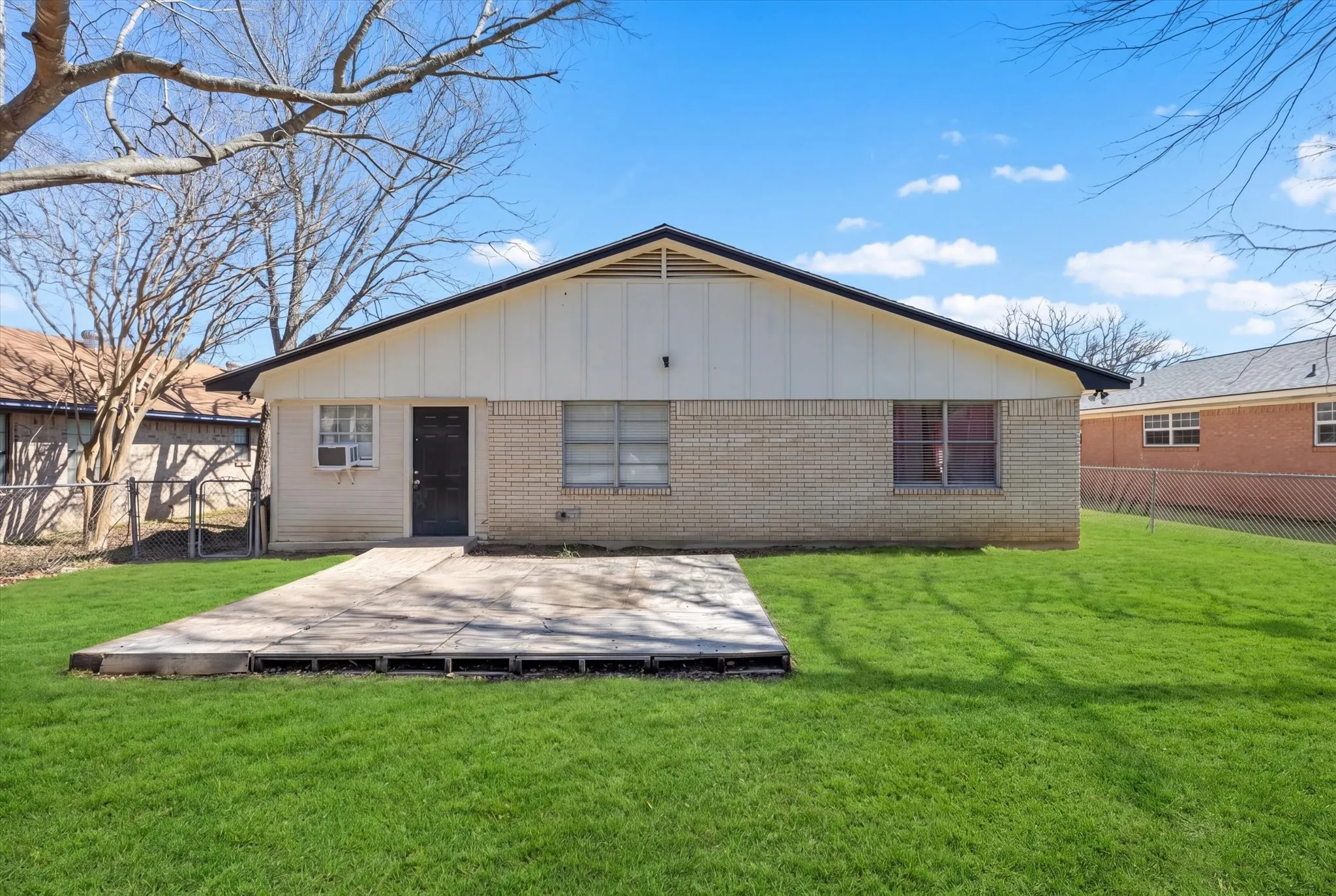 Expansive backyard featuring a concrete patio, green lawn, and brick exterior