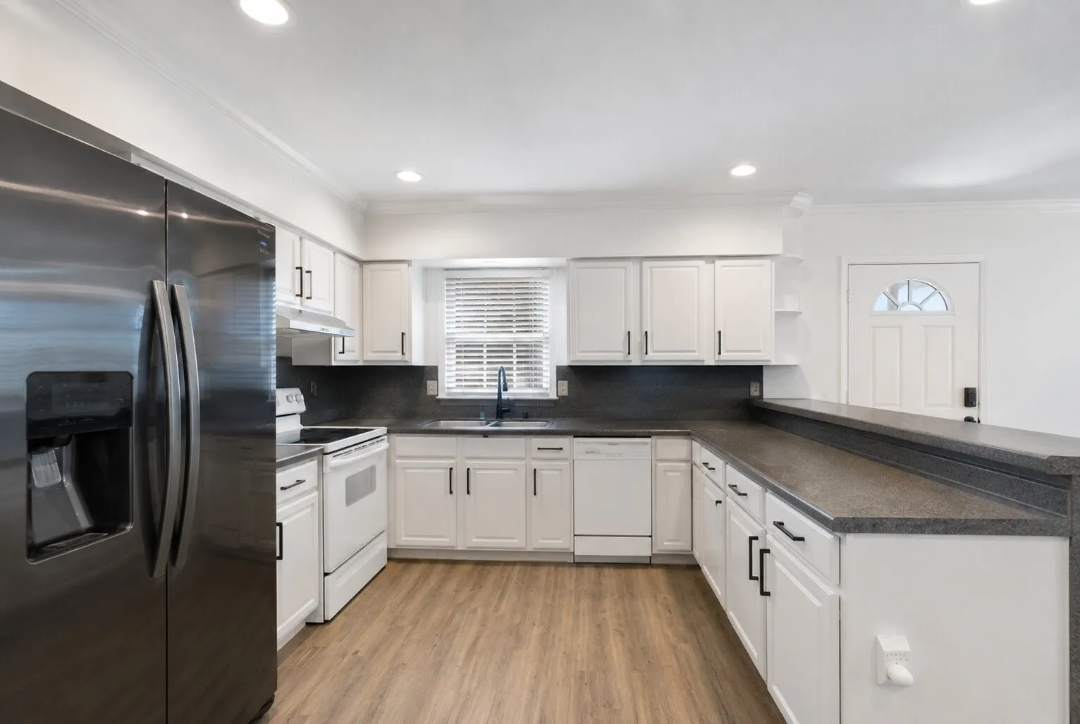 Updated kitchen featuring wood-finish flooring, white cabinetry with black hardware, stainless steel appliances, and dark countertops