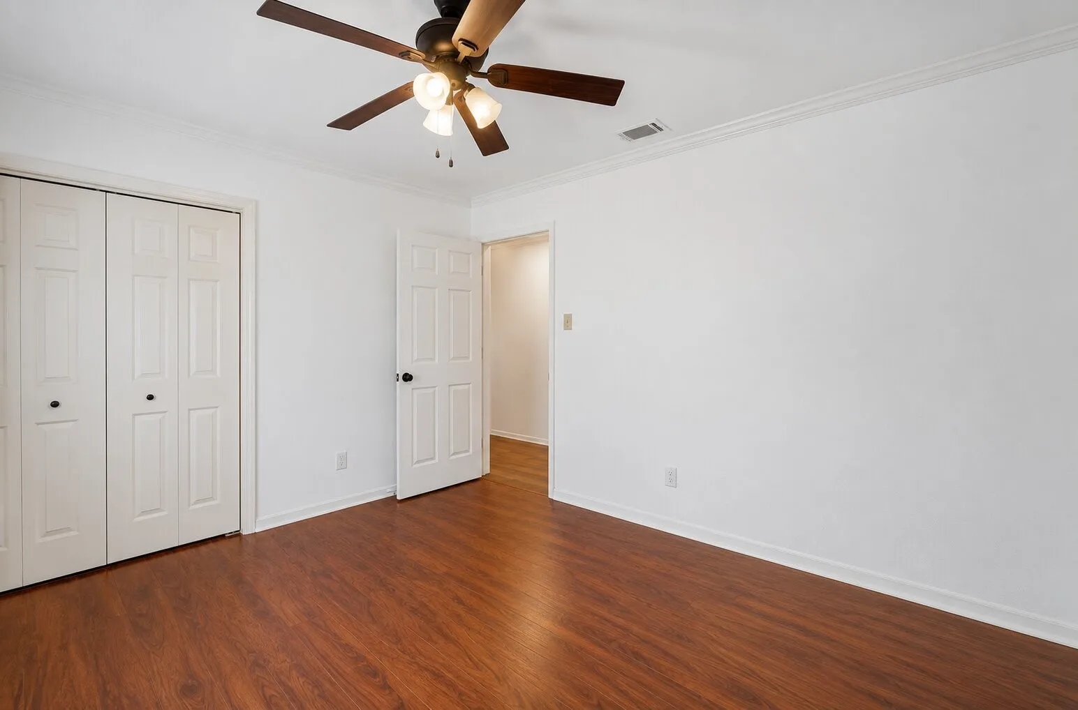 Wood-finish flooring, white walls, white trim, ceiling fan with light fixture, and bifold closet doors