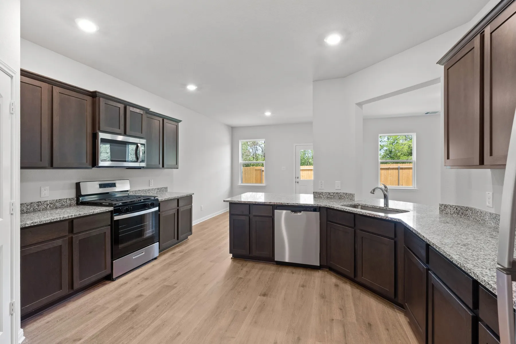 Kitchen featuring appliances with stainless steel finishes, sink, dark brown cabinetry, light stone countertops, and light hardwood / wood-style flooring