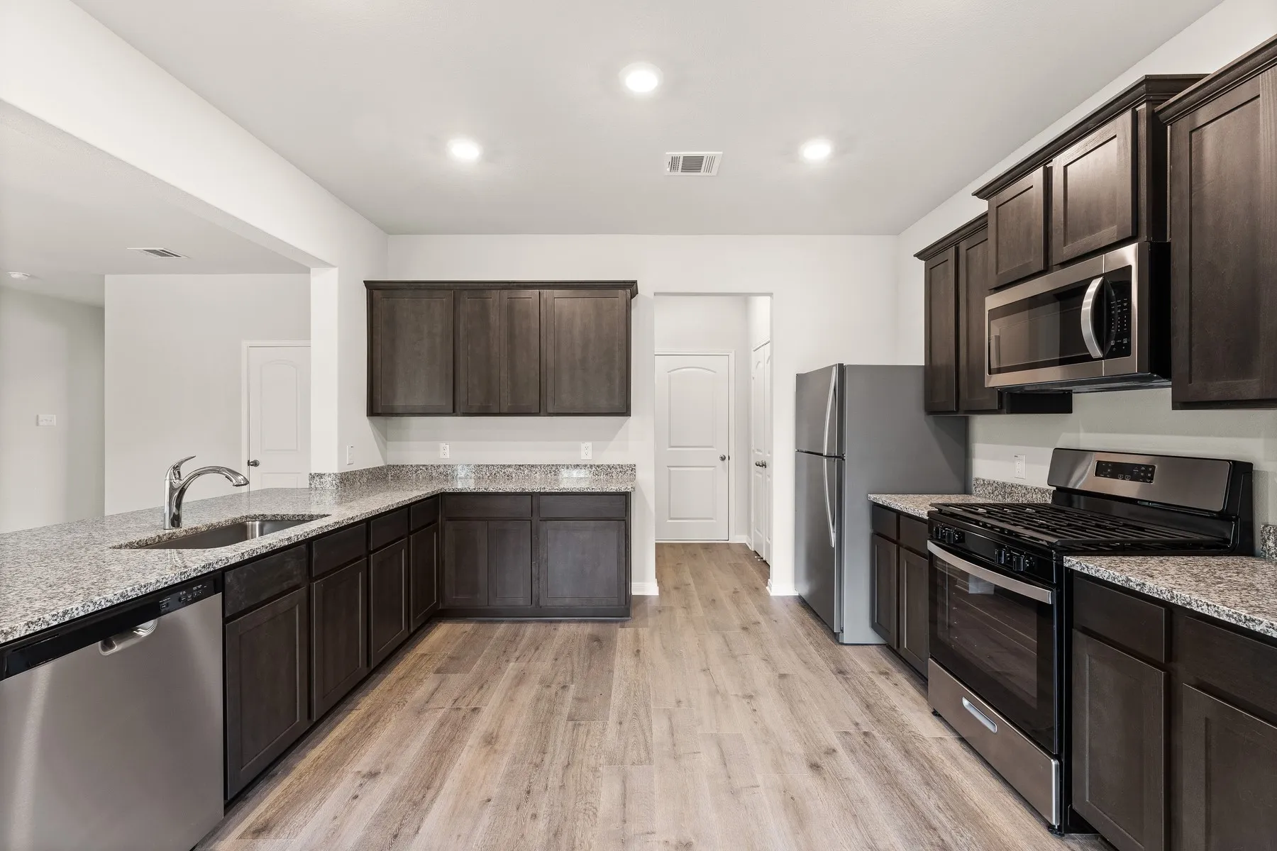 Kitchen featuring stainless steel appliances, dark brown cabinetry, light stone counters, light wood-style flooring, and recessed lighting