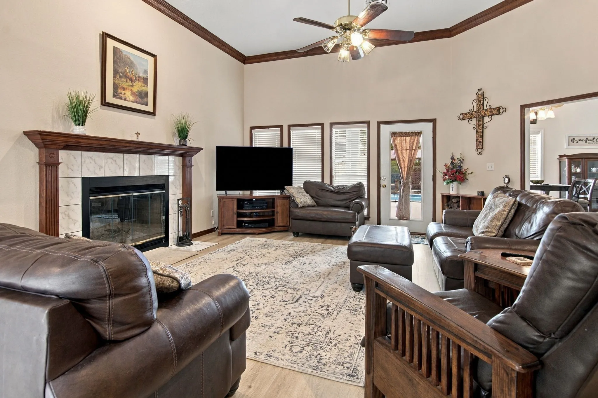 Vaulted ceilings with a ceiling fan, fireplace with a tile surround and wood mantel, wood-finish flooring, and multiple window-door units with privacy blinds