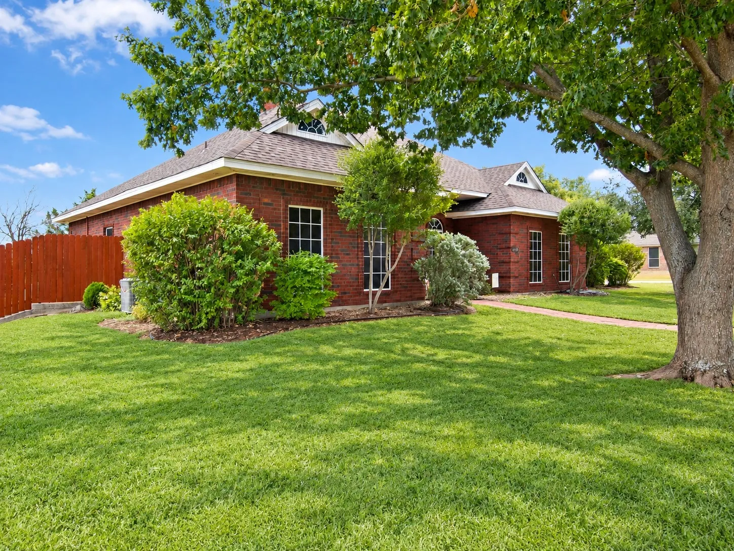 Brick exterior with dormer window, gabled roofline, mature trees, and landscaping *grass greened