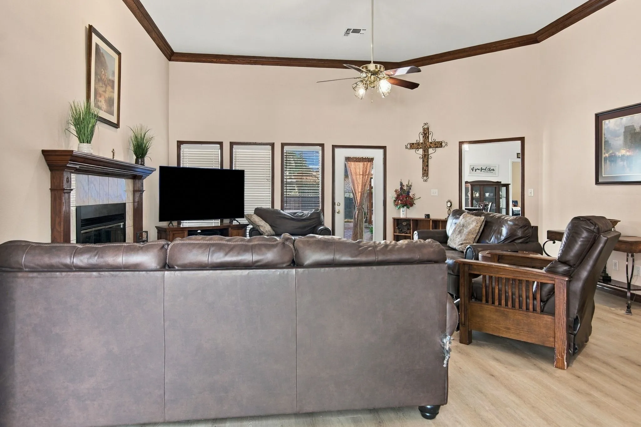 Vaulted ceiling with crown molding, wood-finish flooring, fireplace with wood mantel, and a ceiling fan with integrated lighting