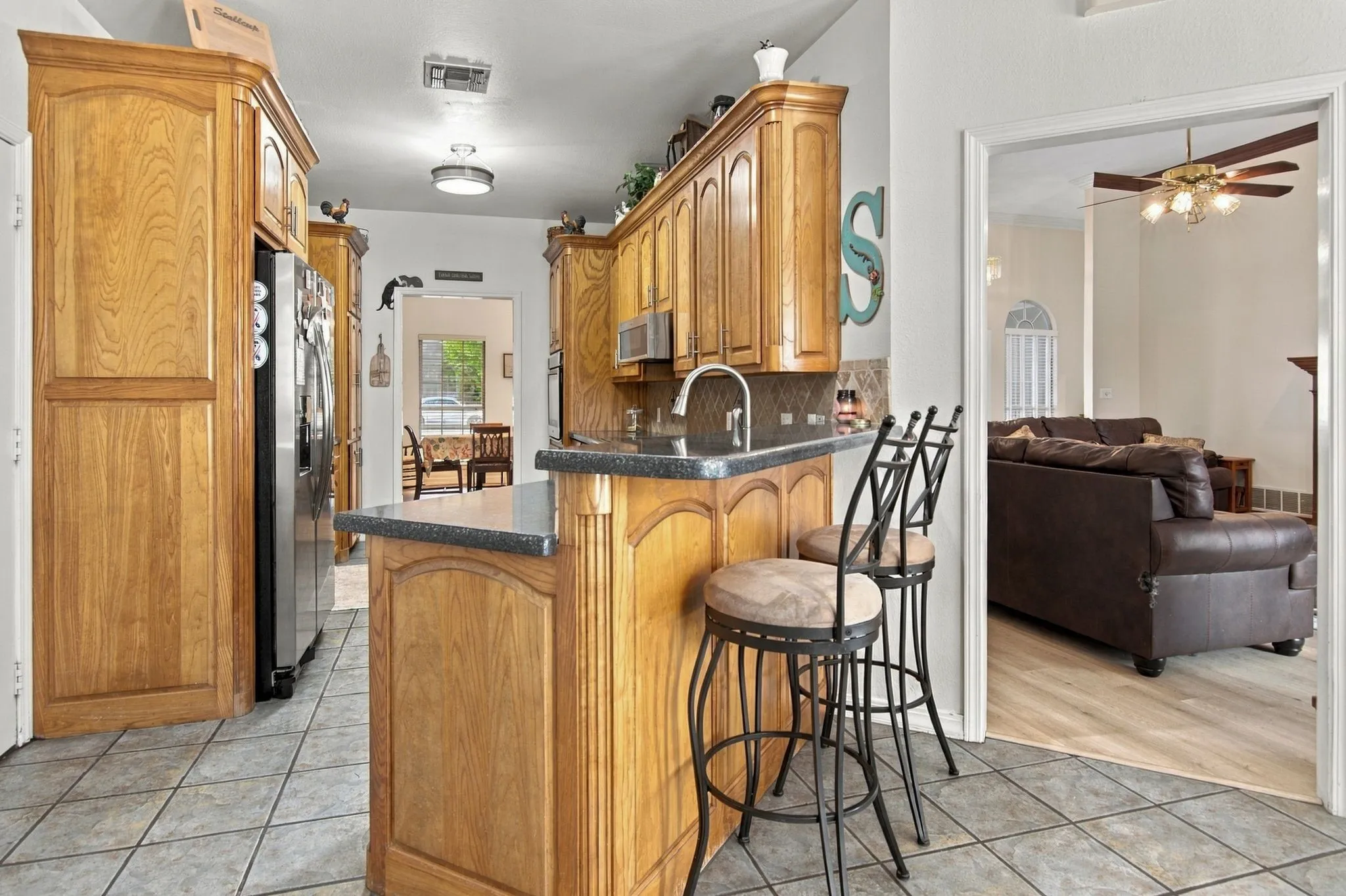 Kitchen featuring wood cabinetry, dark countertops, a built-in oven, and a stainless steel refrigerator