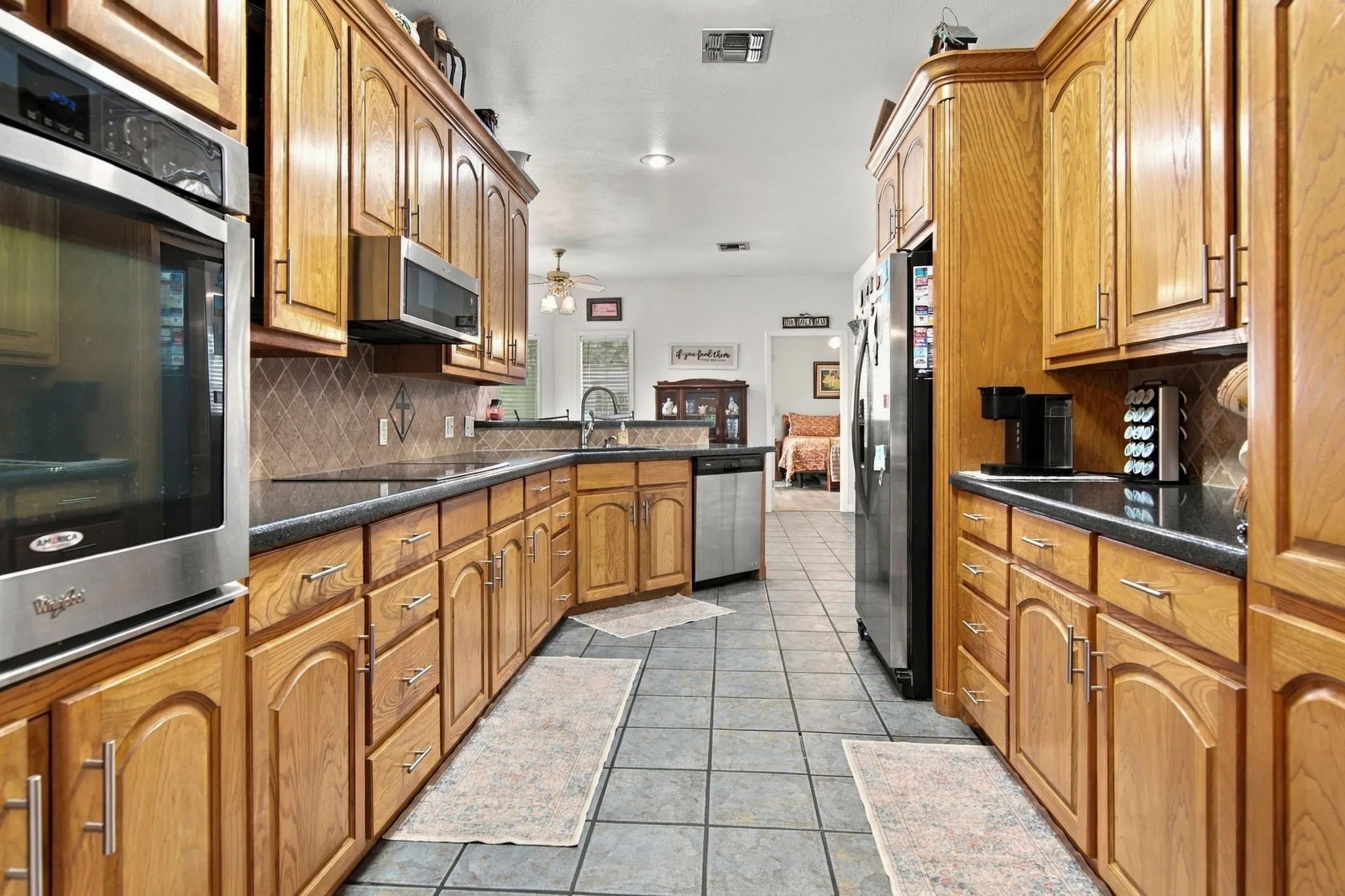 Galley kitchen featuring wood cabinetry, black countertops, stainless steel appliances, and tile flooring