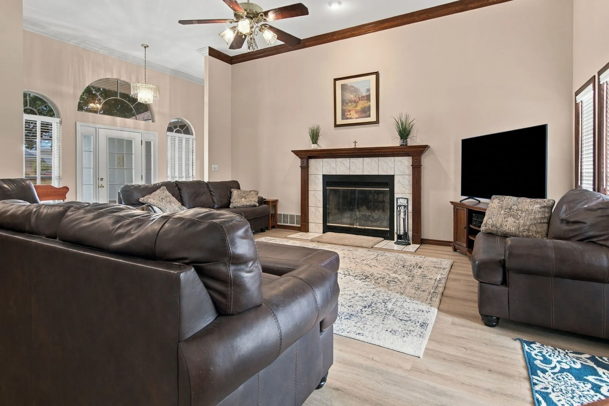 Vaulted ceiling with a ceiling fan, fireplace with a tile surround and wood mantel, wood-finish flooring, and arched windows