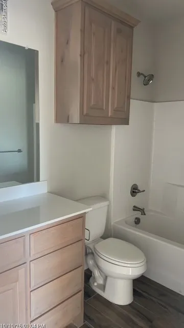Wood-finish vanity with white countertop, complementing wood-finish wall cabinet, and a white tub with shower fixture