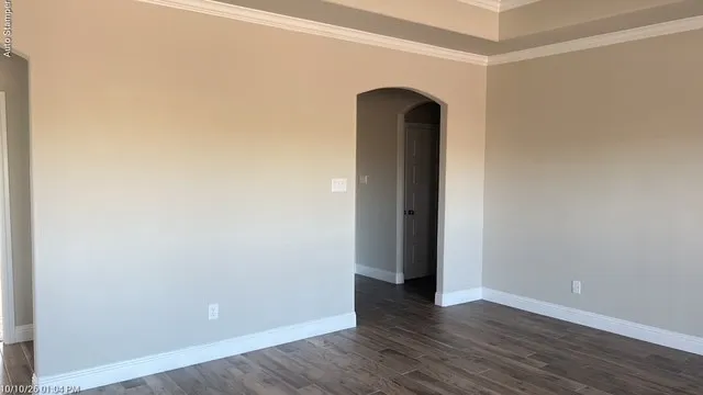 Wood-finish flooring, neutral wall tones, crown molding, white trim, and an arched doorway