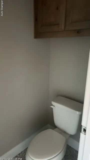 White toilet with patterned floor tile and wood-finish overhead cabinetry