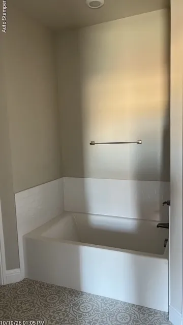 Recessed lighting illuminates a white built-in bathtub with a dark fixture set against white subway tile wainscoting