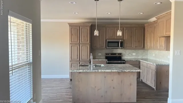 Wood-finish cabinetry with crown molding, stainless steel appliances, central island with seating, pendant lighting, and recessed ceiling lights