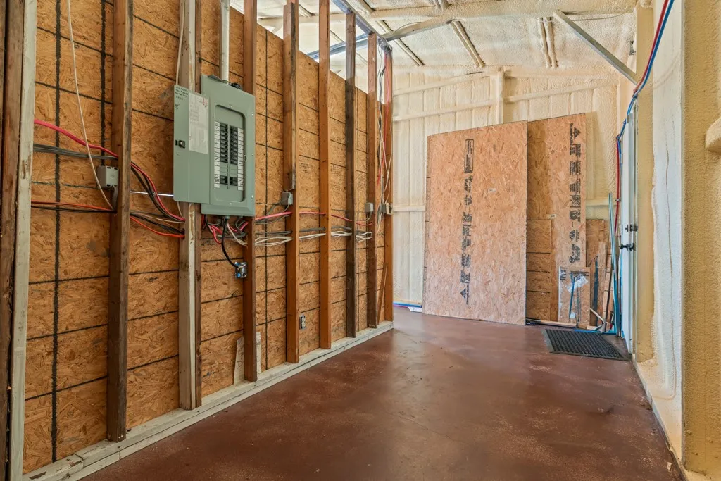 Electrical panel with visible wiring, oriented strand board walls, exposed framing, spray foam insulation, and a concrete floor