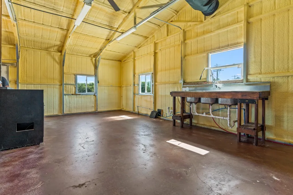 Spacious interior with exposed structural beams, high vaulted ceiling, multiple windows, concrete flooring, and a multi-basin utility sink