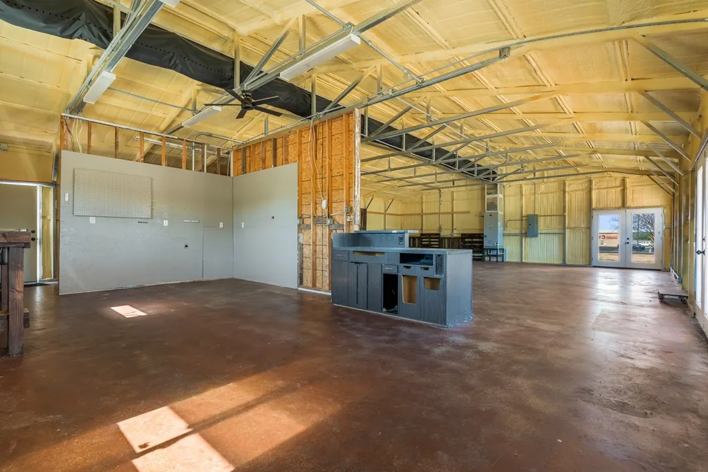 Expansive open interior with exposed structural beams, spray foam insulation, concrete flooring, and double glass doors