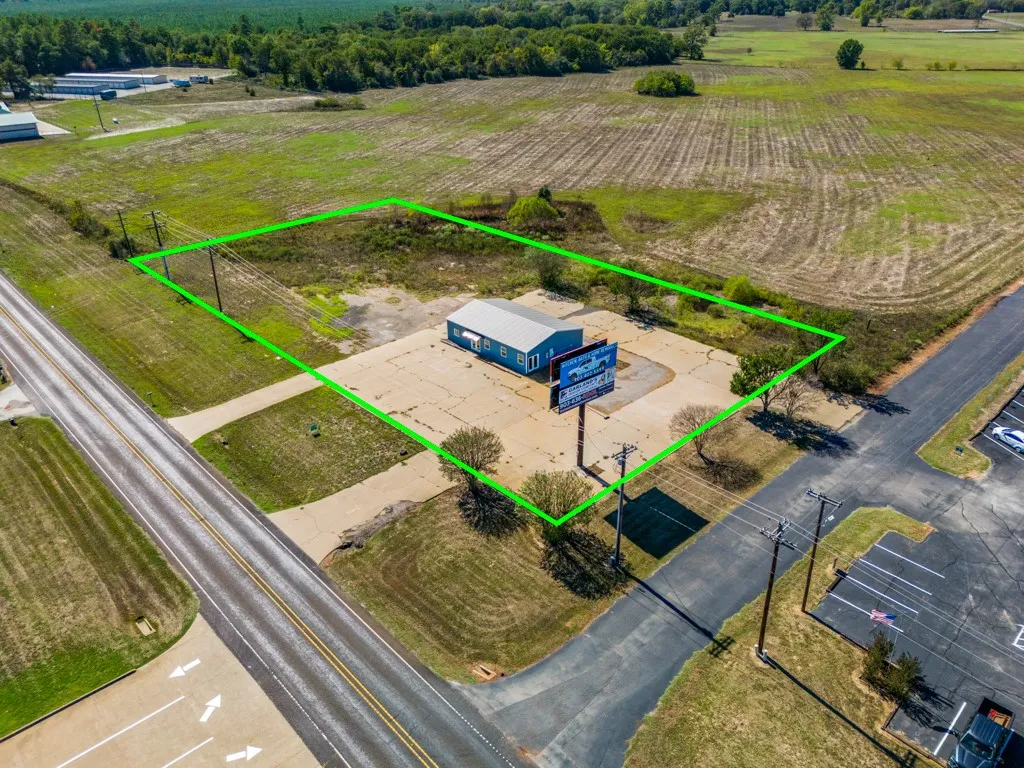 Blue single-story building with a gray metal roof, expansive paved lot, and direct road frontage