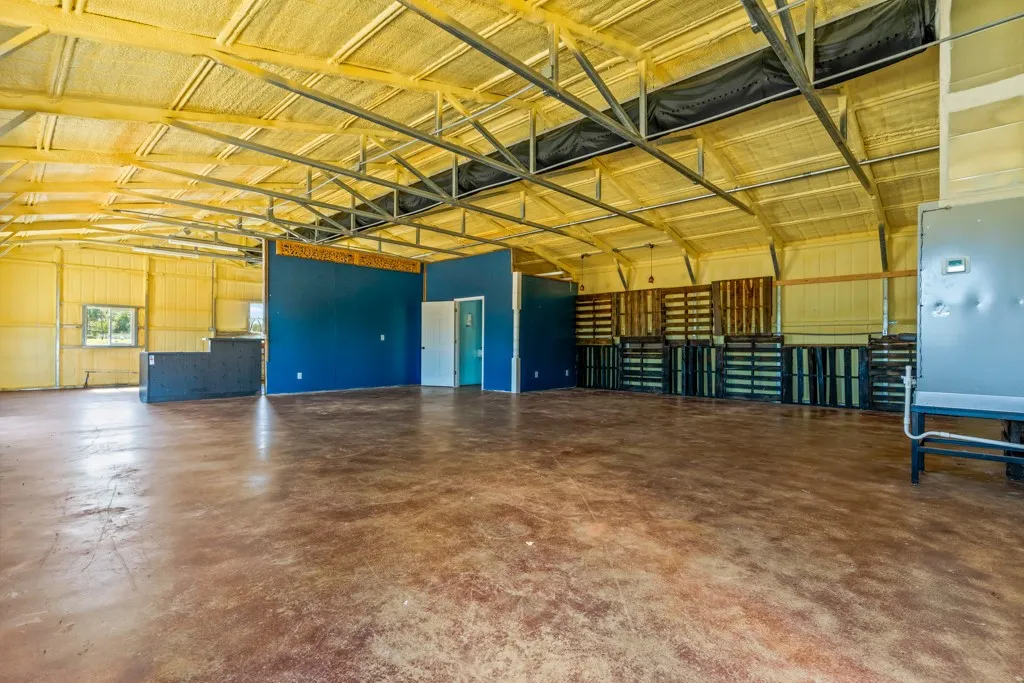 Expansive open space featuring exposed metal truss ceilings, concrete flooring, and insulated walls