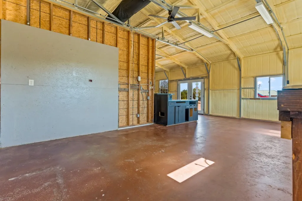 Vaulted ceiling with exposed metal beams, dual ceiling fans, multiple windows, and a set of double doors
