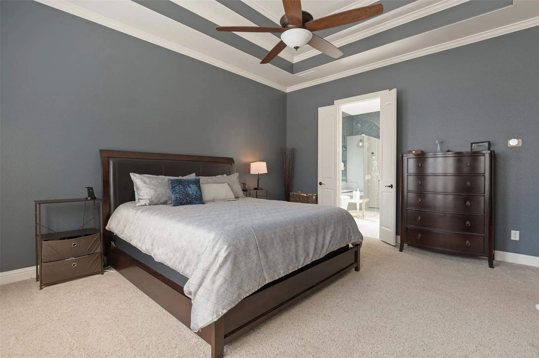 Tray ceiling with crown molding, ceiling fan, carpeting, and double doors opening to an adjoining room
