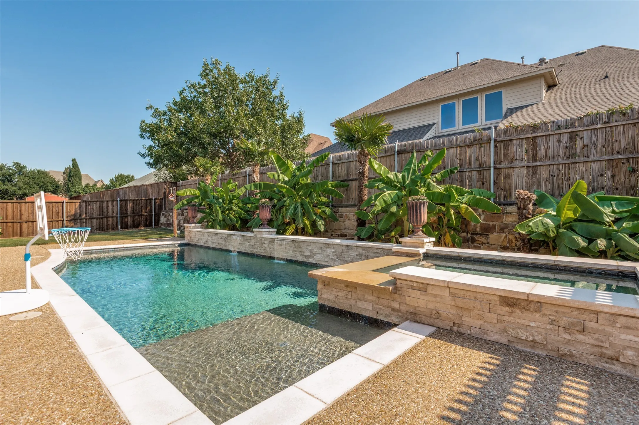 Swimming pool with a spa, stone-clad retaining walls, and surrounding landscaping