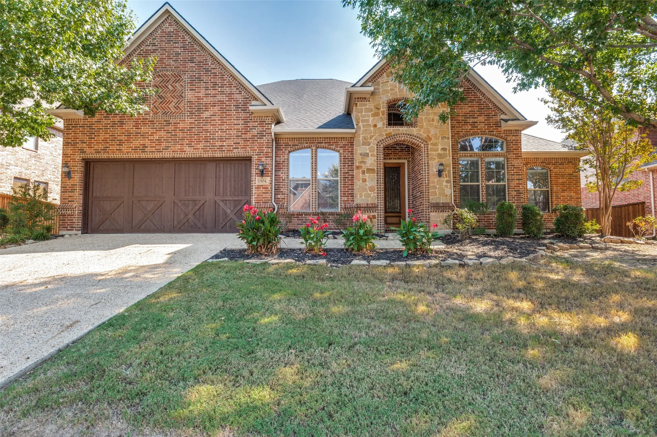 Brick and stone exterior featuring an arched entryway, decorative garage door, and mature landscaping