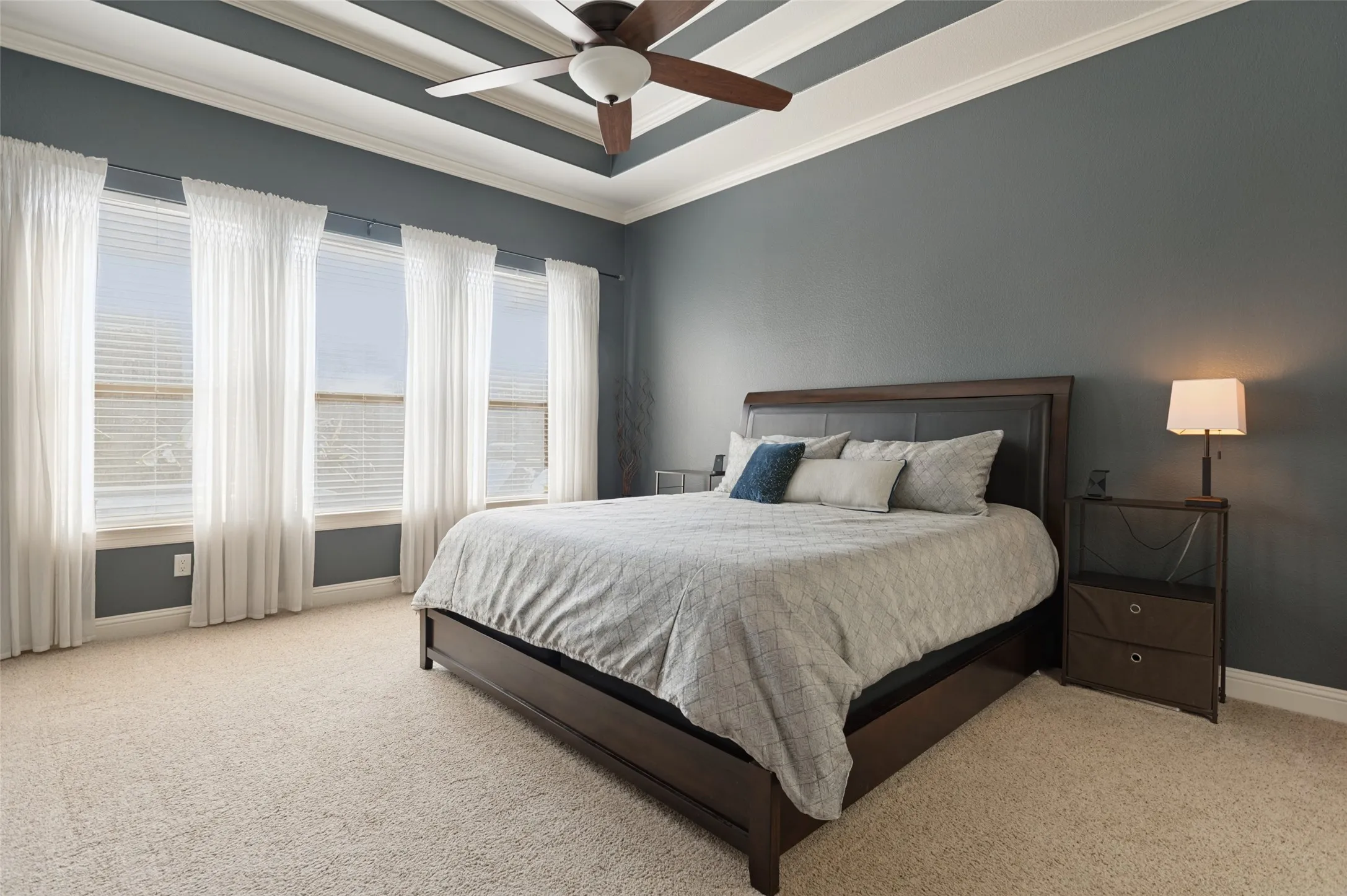 Tray ceiling with a ceiling fan, wall-to-wall carpeting, multiple windows, and a dark wall finish