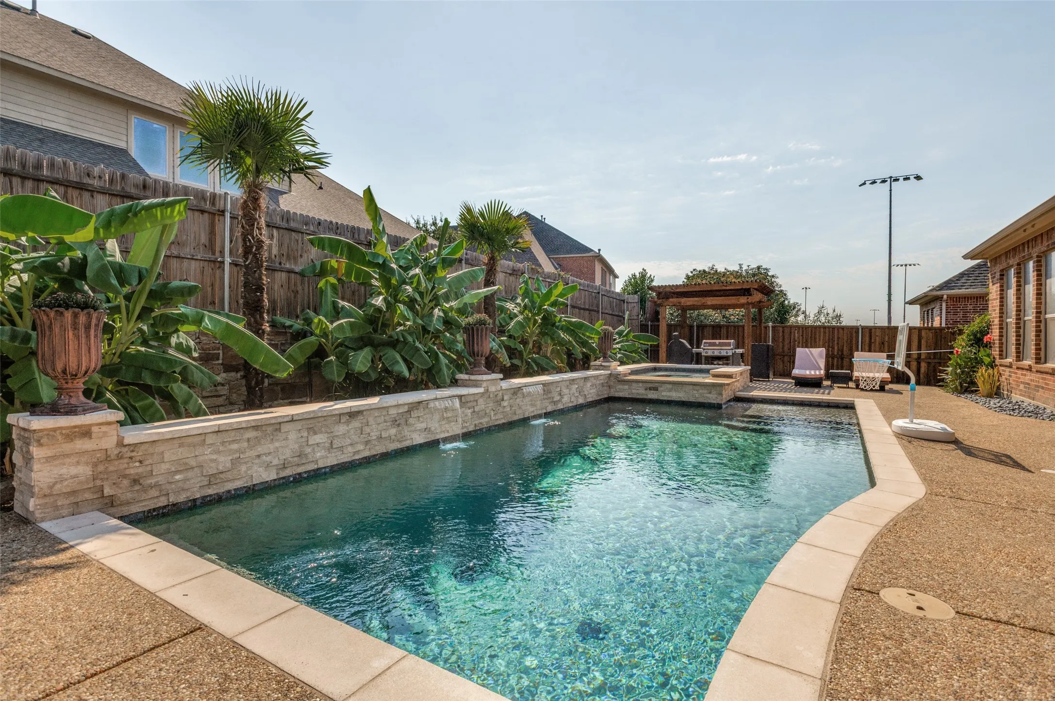 In-ground pool with stone coping, integrated spa, and a flagstone-clad raised planter with mature tropical landscaping