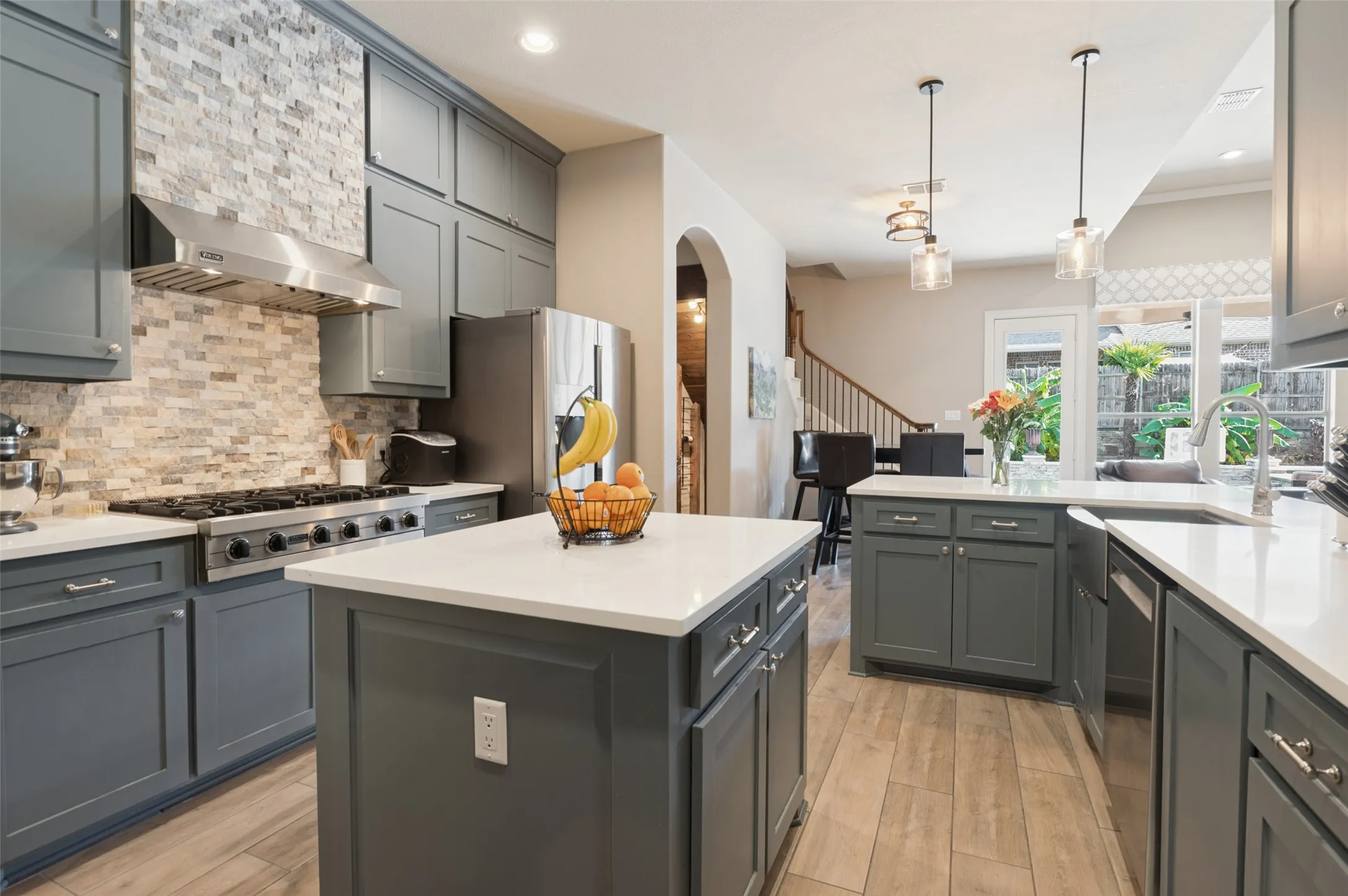 Kitchen featuring extensive cabinetry, stone backsplash, stainless steel range with hood, two islands with solid countertops, and wood-finish flooring