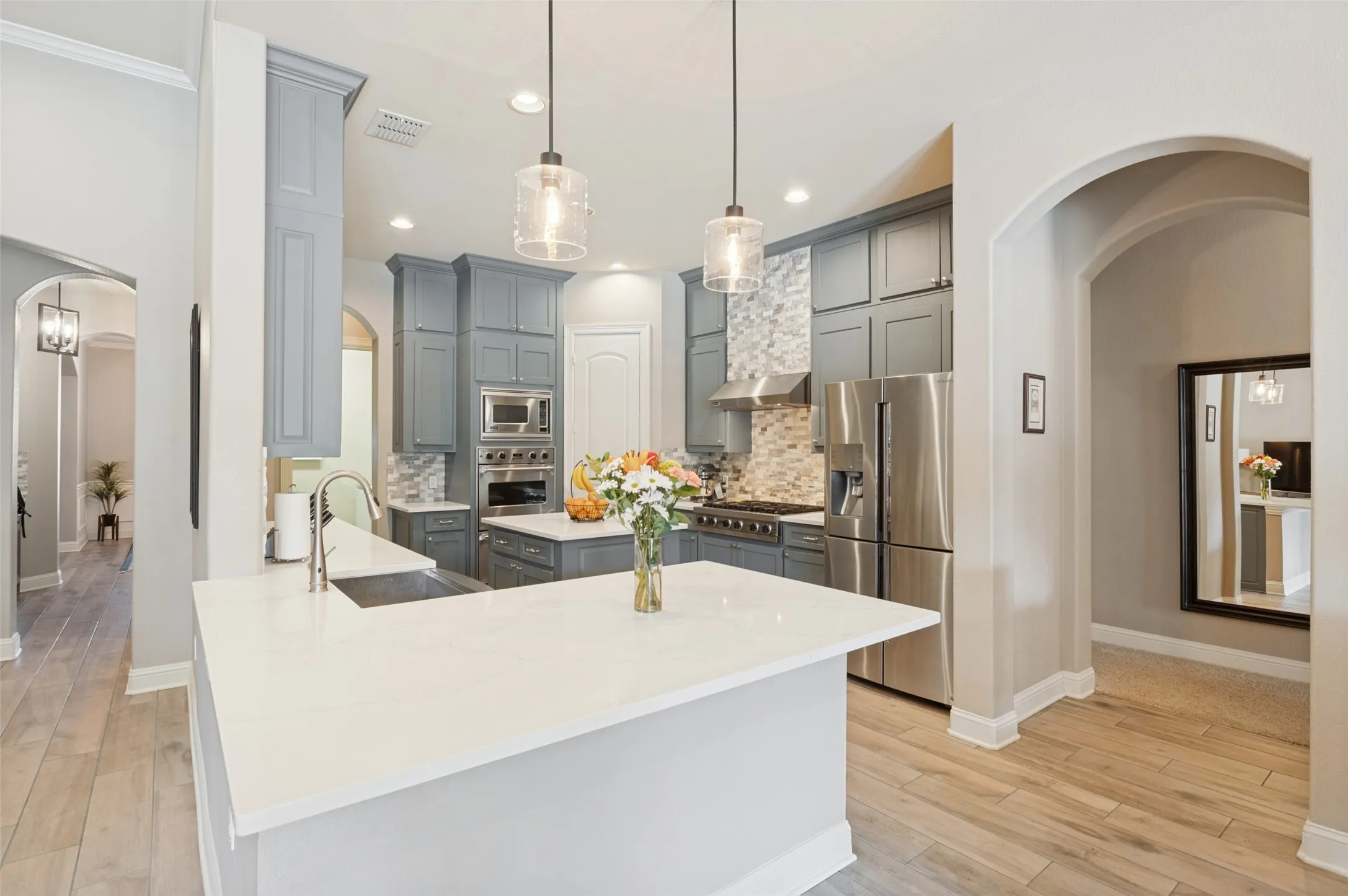 Kitchen featuring light grey cabinetry, stainless steel appliances, a white island, contemporary pendant lighting, and wood-finish flooring