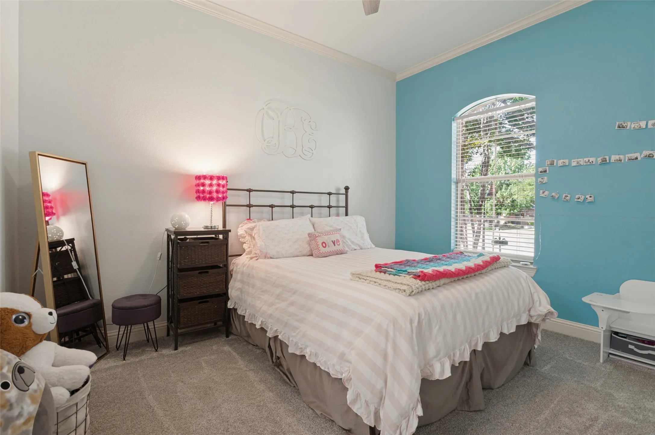 Arch-top window with blinds, wrought iron bed frame, crown molding, and carpeted flooring