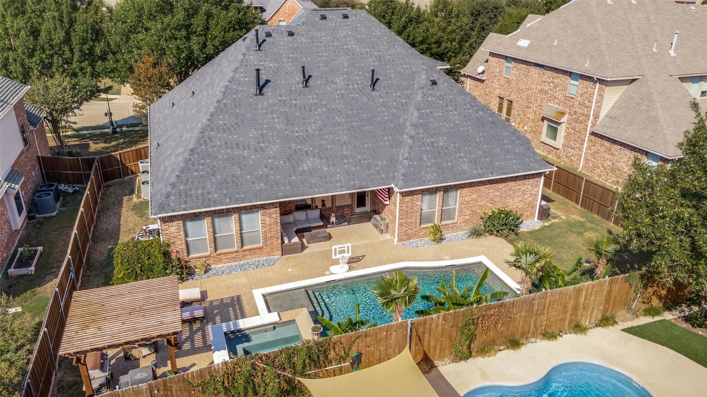 Brick exterior with a dark shingle roof, a concrete patio, and an in-ground swimming pool