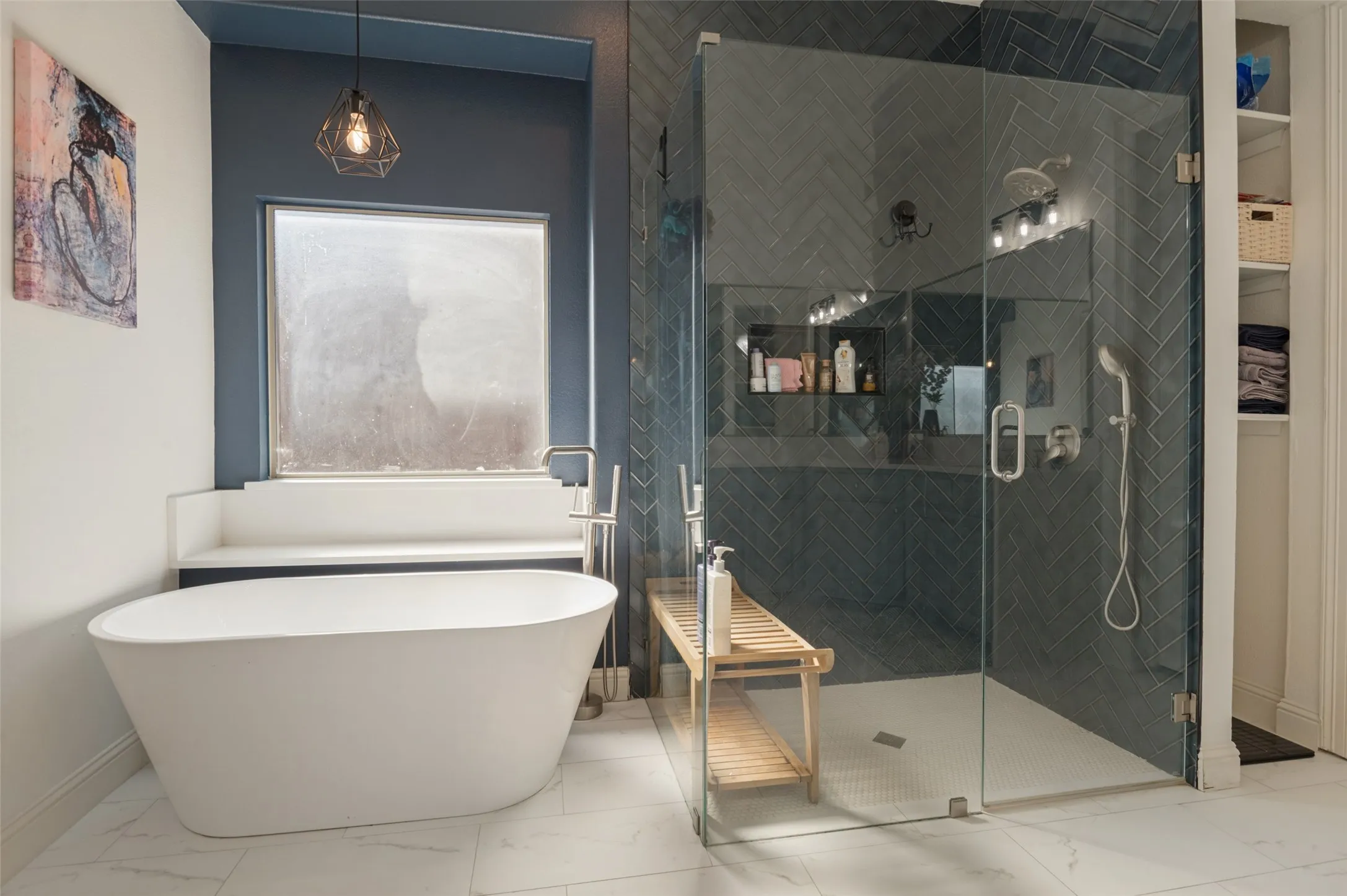 Freestanding soaking tub, glass-enclosed shower with herringbone tile, built-in shower niche, and white marble-look flooring