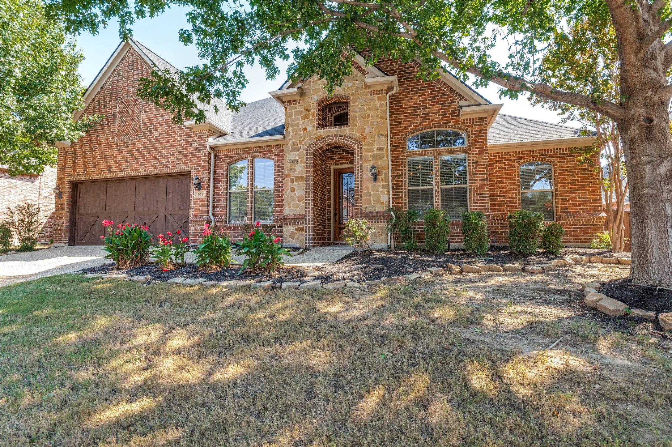 Brick and stone exterior with an arched entryway, decorative garage door, and well-maintained​​‌​​​​‌​​‌‌​‌‌​​​‌‌​‌​‌​‌​​​‌​​ shrubbery