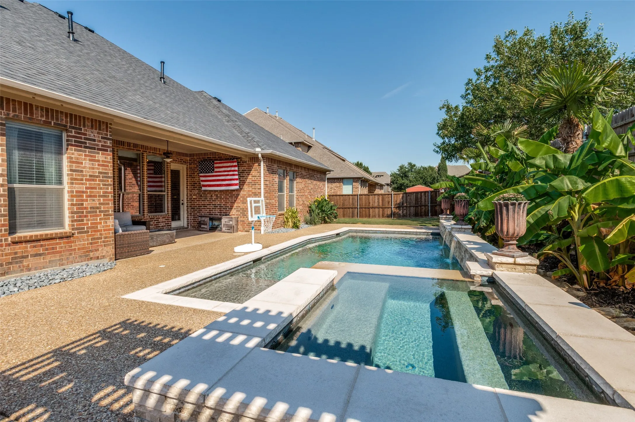 Brick exterior with a covered patio, exposed aggregate patio, and an in-ground swimming pool with an integrated spa