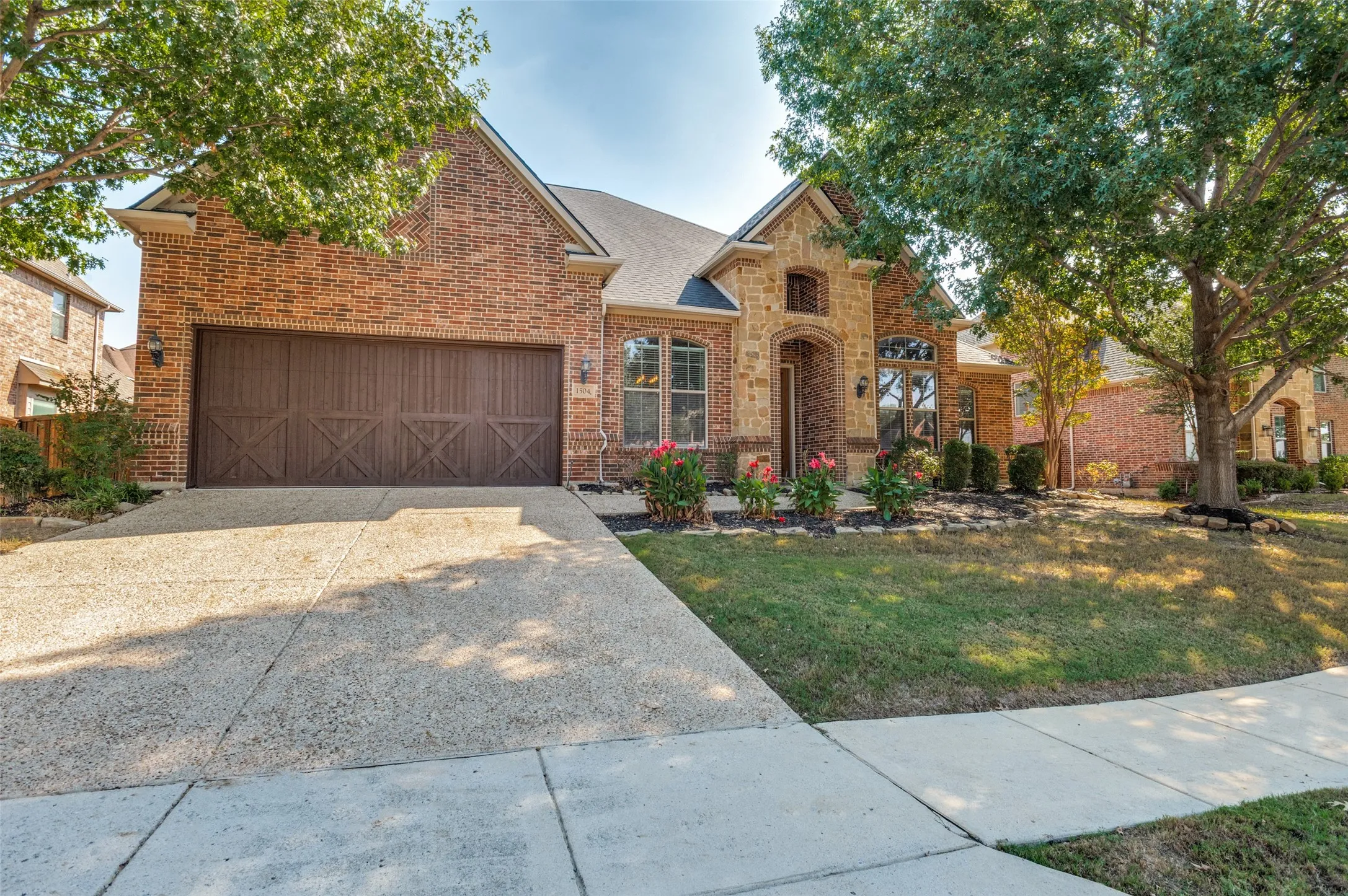 Brick exterior with stone accents, arched entryway, decorative wood garage door, concrete driveway, and established landscaping