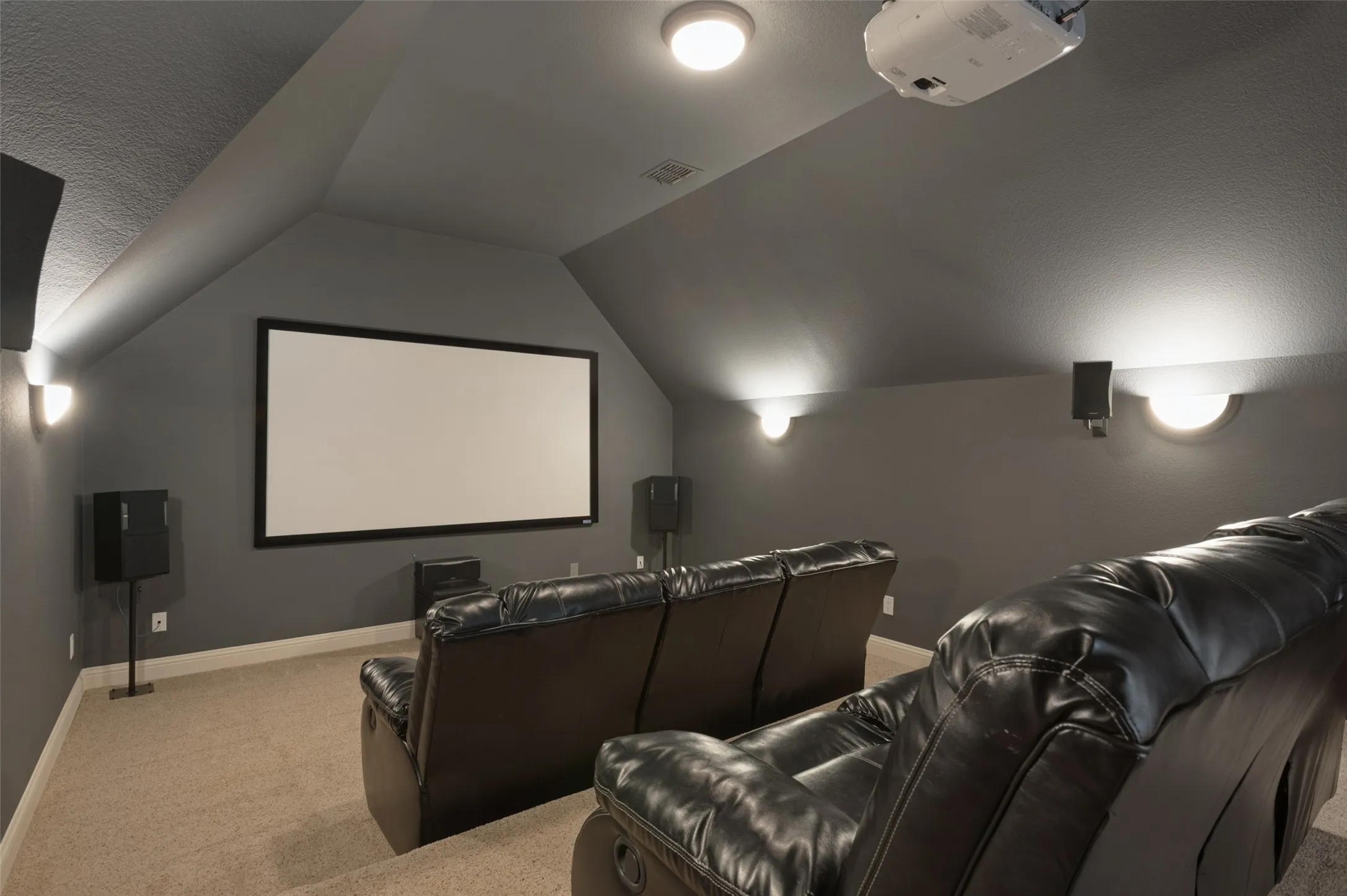 Dedicated media room featuring a large projection screen, wall-mounted speakers, recessed lighting, and sconce lighting