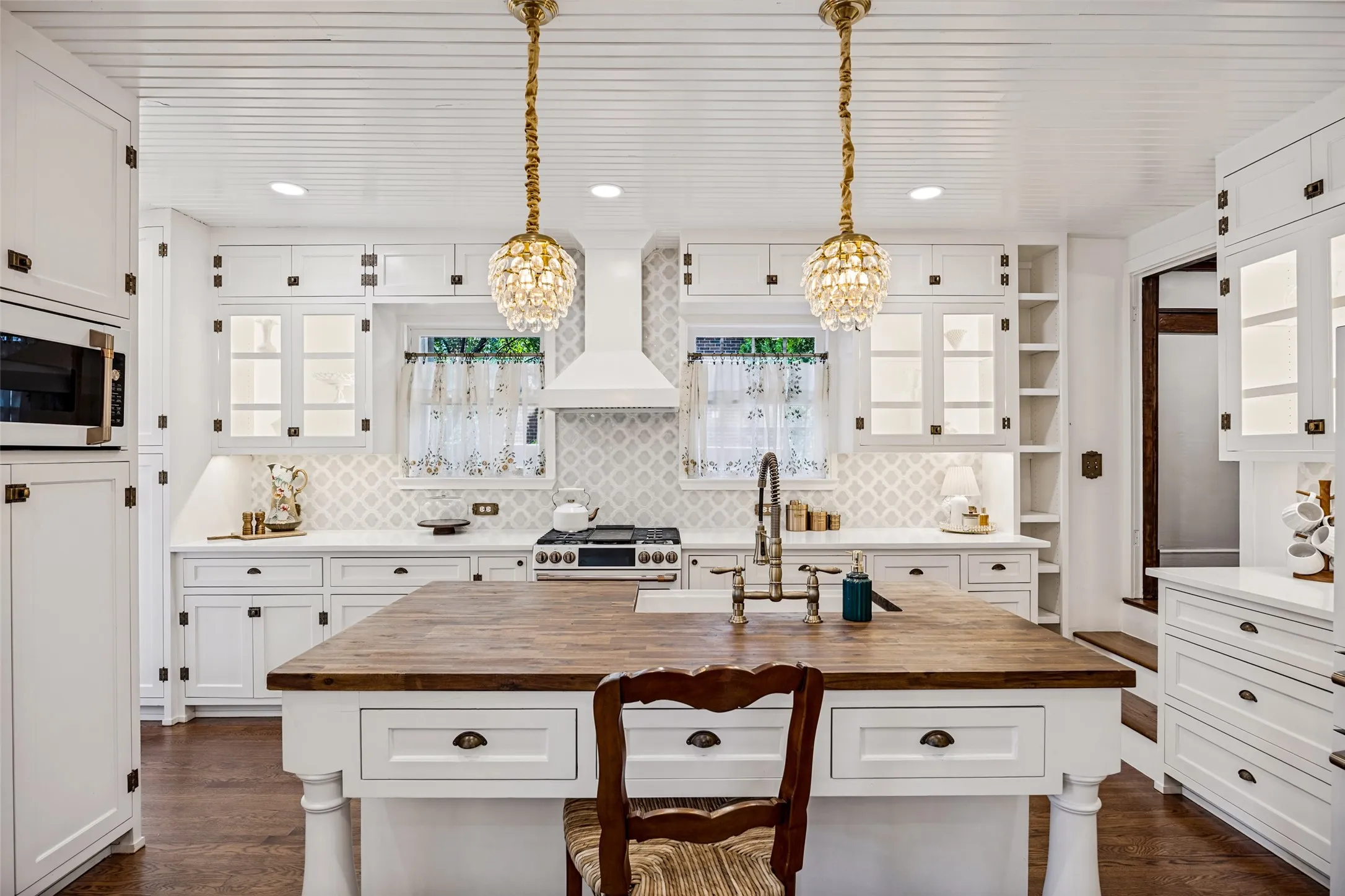 Spacious kitchen with a central wood-finish island, white cabinetry, integrated microwave, and a decorative tile backsplash