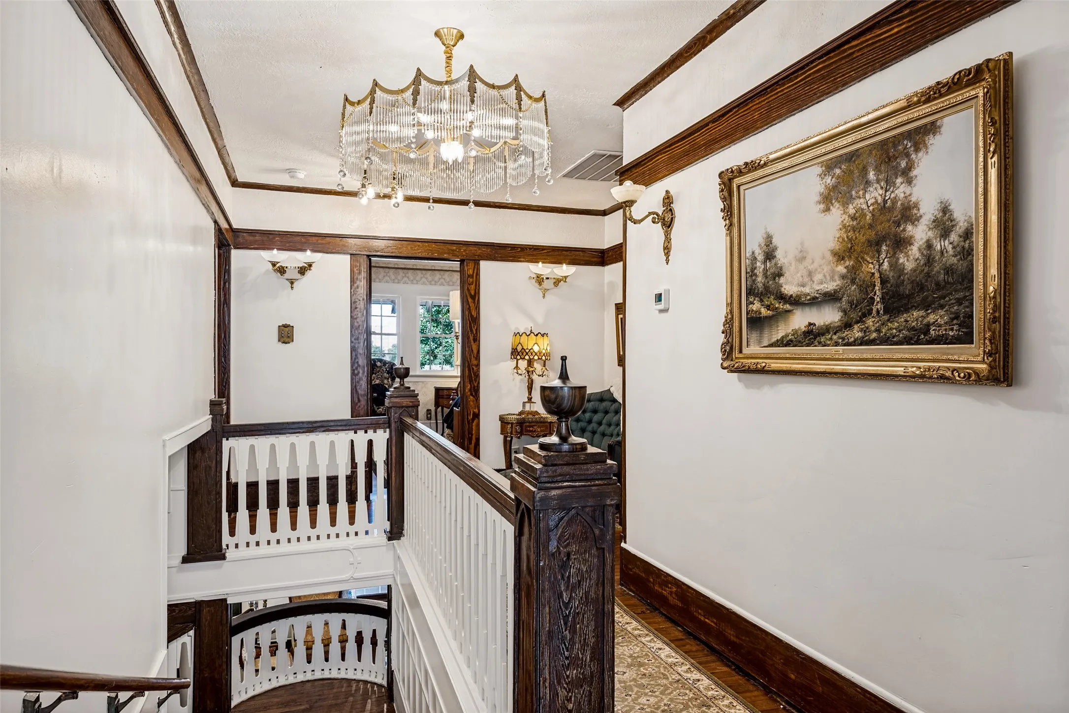 Ornate chandelier, dark wood trim, white balusters, and a decorative wall sconce