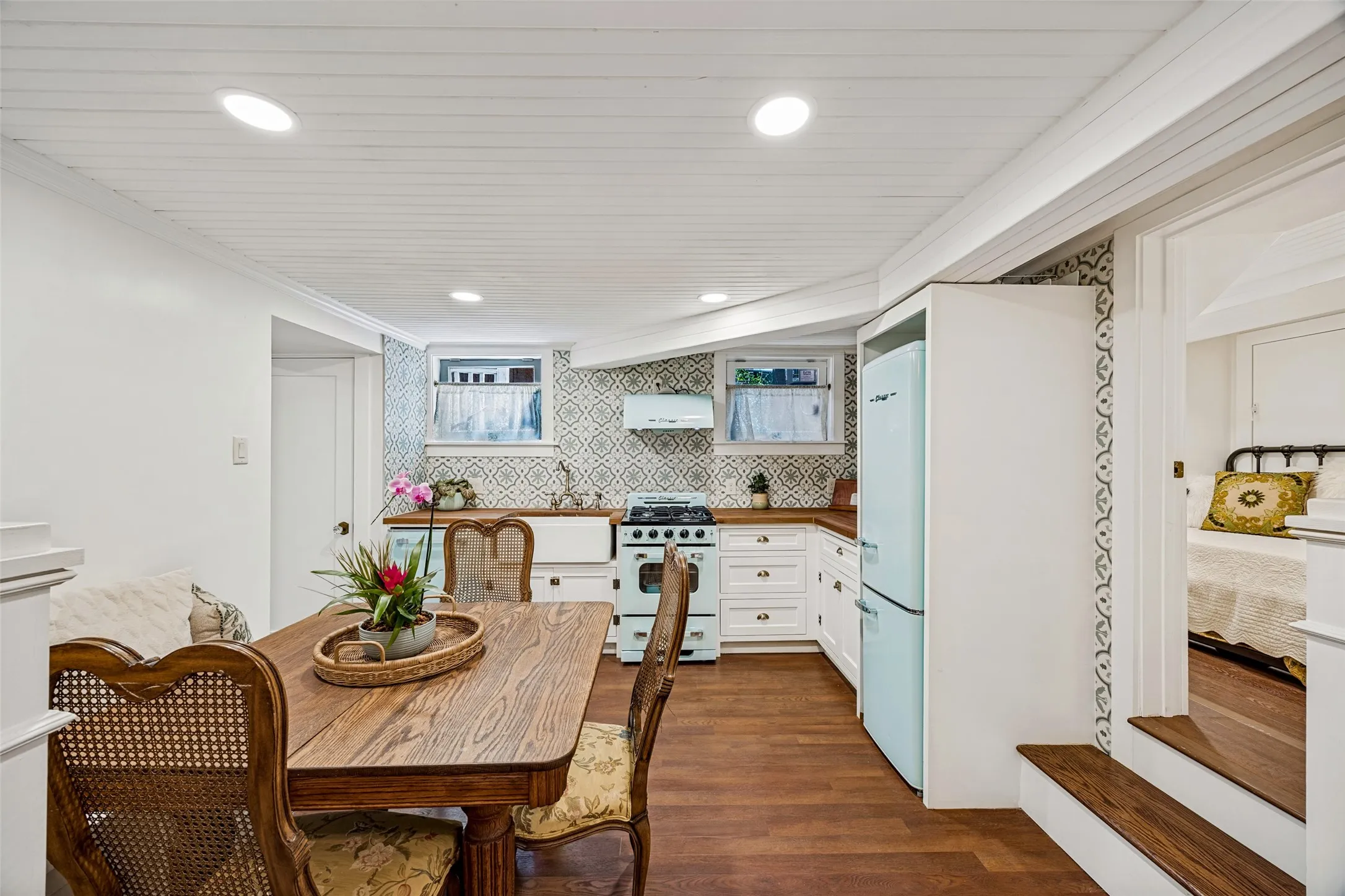 Full kitchen in basement Wood-finish flooring, recessed lighting, white wood panel ceiling, kitchen with white cabinetry, wood countertops, patterned tile backsplash, and a farmhouse sink
