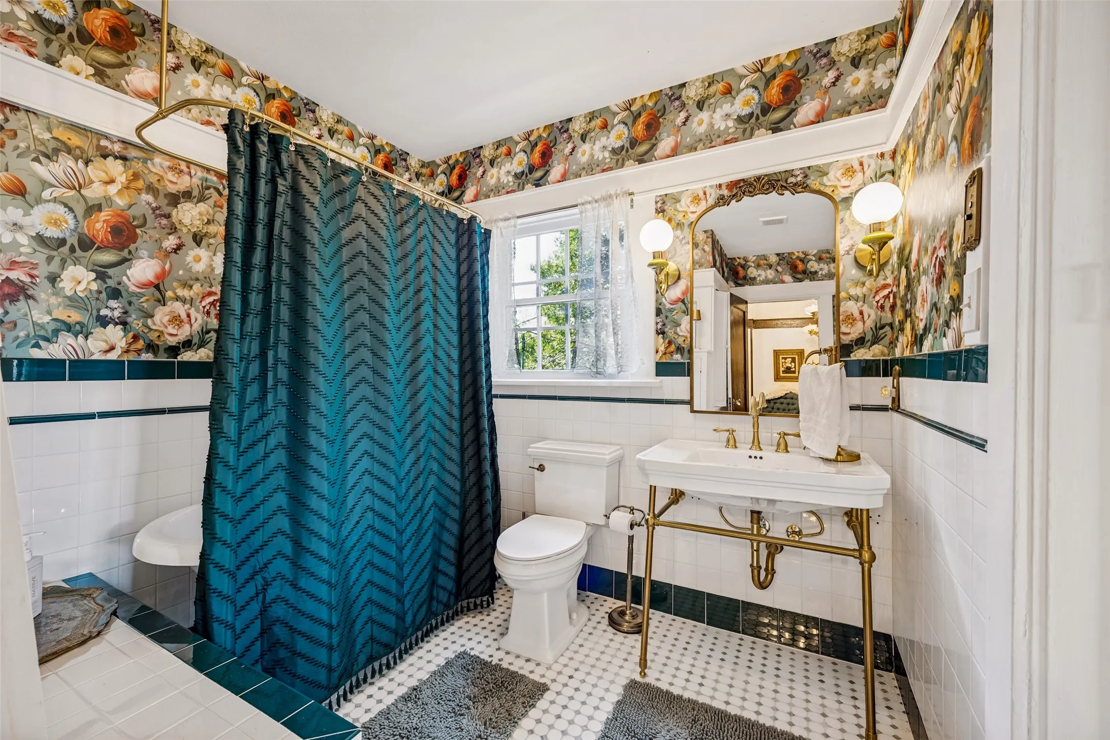 Pedestal sink with brass-finish legs and fixtures, ornate framed mirror with sconce lighting, and patterned wallpaper