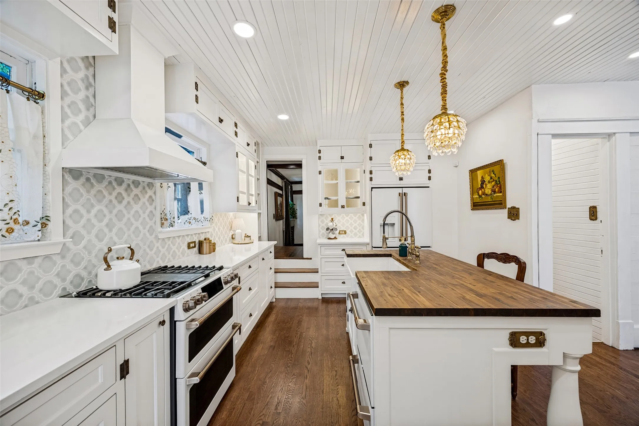 White shaker cabinetry with dark hardware, full backsplash featuring patterned tiles, stainless steel range with double ovens, and a wood-finish island countertop