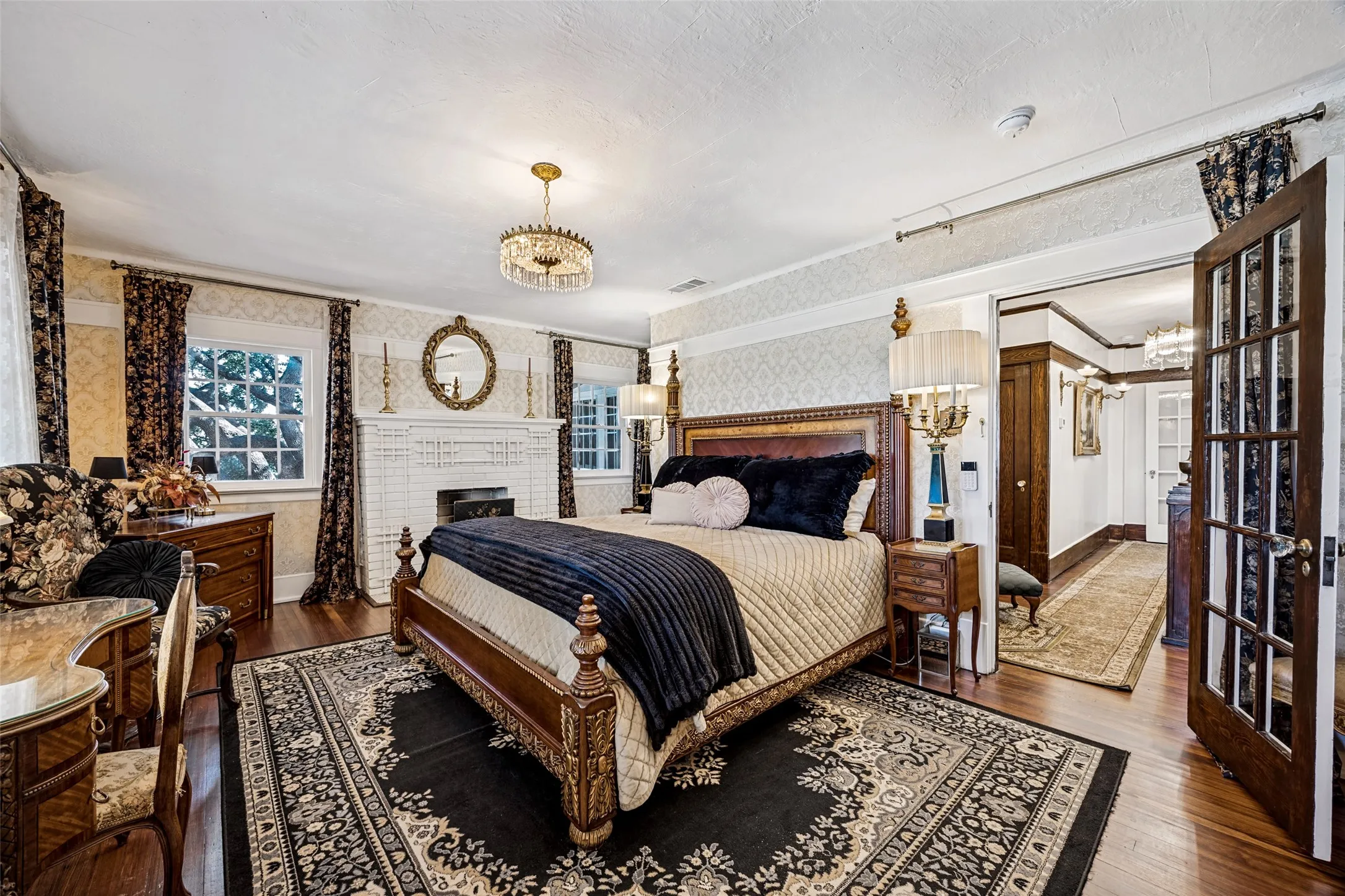 Hardwood flooring, decorative fireplace, crystal chandelier, double french doors, and patterned wallpaper