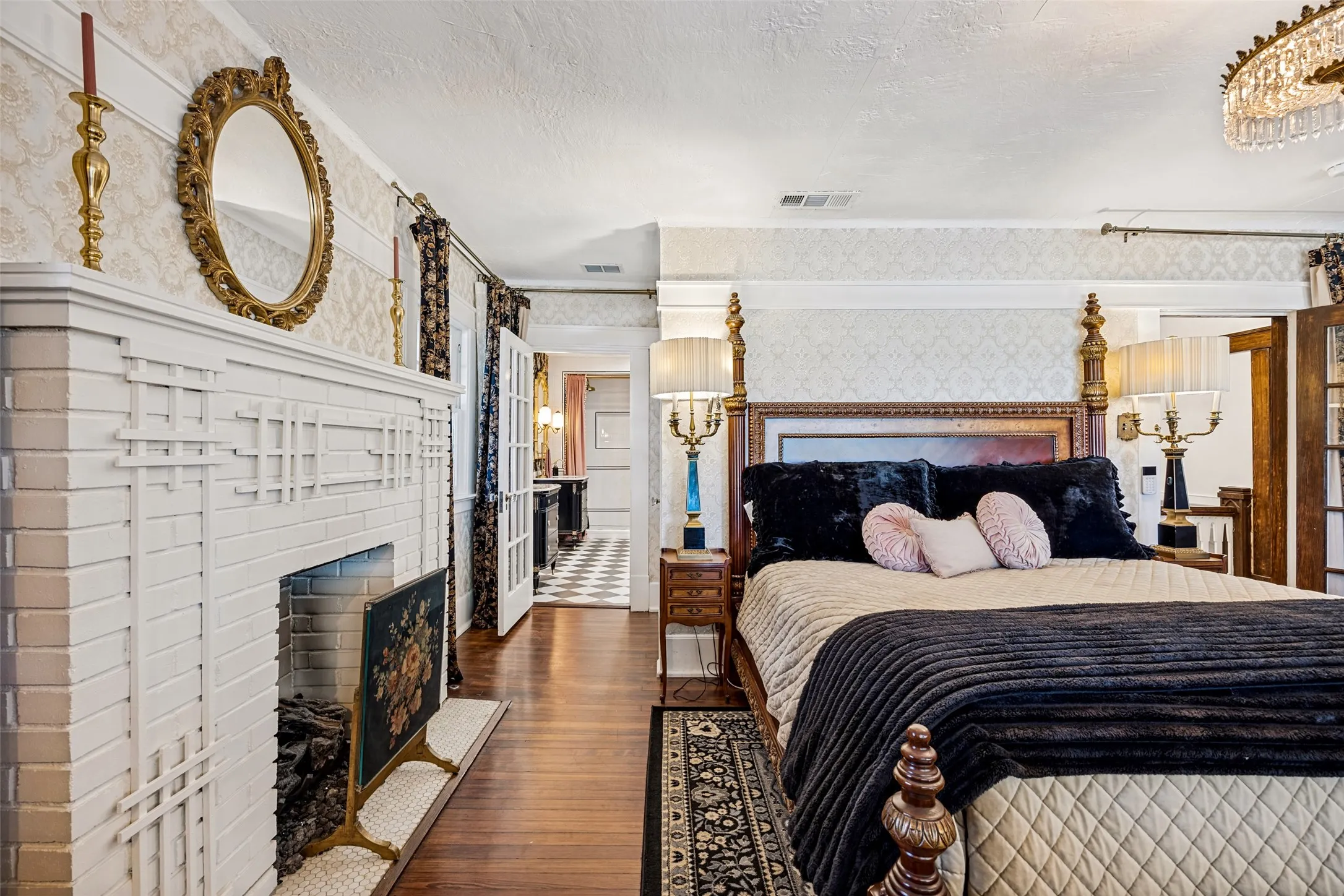 Hardwood flooring, painted brick fireplace with decorative screen, patterned wallpaper, double French doors, and an ornate chandelier